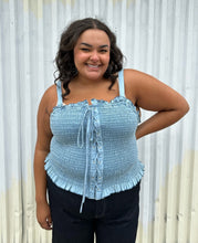 Load image into Gallery viewer, Front view of a size 2 Fashion to Figure chambray all-over smocked tank with a corset-style lace up front styled over dark wash denim on a size 18/20 model. The photo was taken outside in natural lighting.
