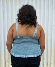 Load image into Gallery viewer, Back view of a size 2 Fashion to Figure chambray all-over smocked tank with a corset-style lace up front styled over dark wash denim on a size 18/20 model. The photo was taken outside in natural lighting.
