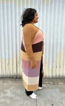 Load image into Gallery viewer, Full-body side view of a size XL (fits comfy up to 22) Free People brown, cream, pink, and purple striped longline open knit cardigan sweater styled open over a light brown top. dark wash denim, and white mules on a size 18/20 model. The photo was taken outside in natural lighting.
