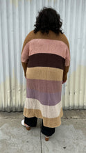 Load image into Gallery viewer, Full-body back view of a size XL (fits comfy up to 22) Free People brown, cream, pink, and purple striped longline open knit cardigan sweater styled open over a light brown top. dark wash denim, and white mules on a size 18/20 model. The photo was taken outside in natural lighting.
