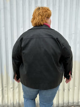 Load image into Gallery viewer, Back view of a size 48 Noisy May black faux leather moto jacket styled open over a pink cropped turtleneck and medium wash denim on a size 22/24 model. The photo was taken outside in natural lighting.
