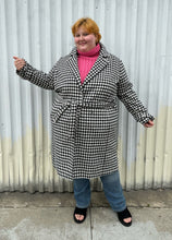 Load image into Gallery viewer, Full-body front view of a size 22 Vero Moda black and white houndstooth plaid belted peacoat styled tied closed over a pink turtleneck and medium wash denim on a size 22/24 model. The photo was taken outside in natural lighting.
