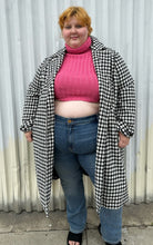 Load image into Gallery viewer, Front view of a size 22 Vero Moda black and white houndstooth plaid belted peacoat styled open over a pink turtleneck and medium wash denim on a size 22/24 model. The photo was taken outside in natural lighting.
