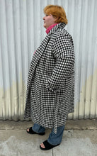 Load image into Gallery viewer, Full-body side view of a size 22 Vero Moda black and white houndstooth plaid belted peacoat styled tied closed over a pink turtleneck and medium wash denim on a size 22/24 model. The photo was taken outside in natural lighting.
