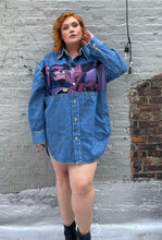 Load image into Gallery viewer, Full-body front view of a size XL Lanvin painted Batman denim button-up styled closed like a mini dress on a size 18 model. The photo is taken outside in natural lighting.
