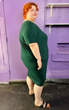 Load image into Gallery viewer, Full-body side view of a size L Universal Standard emerald green v-neck caftan midi dress styled with black and brown sandals on a size 22/24 model. The photo was taken inside under flourescent and natural lighting.
