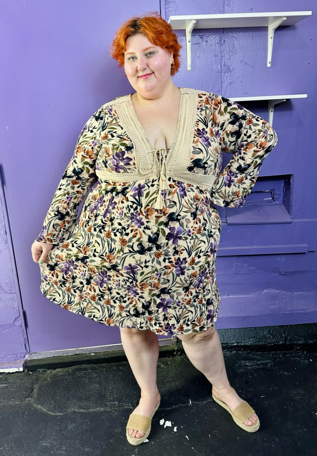Full-body front view of a size 3 Torrid light tan, orange, purple, and black floral crochet embroidered detail 70s inspired long sleeve midi dress on a size 22/24 model. The photo was taken inside in flourescent and natural lighting.