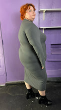 Load image into Gallery viewer, Full-body side view of a size 3X Finesse dark gray ribbed long sleeve midi dress with a shoulder cut out, two front slits, and contrast stitching details styled with patent leather black boots on a size 22/24 model. The photo was taken inside in flourescent and natural lighting.
