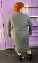 Load image into Gallery viewer, Full-body back view of a size 3X Finesse dark gray ribbed long sleeve midi dress with a shoulder cut out, two front slits, and contrast stitching details styled with patent leather black boots on a size 22/24 model. The photo was taken inside in flourescent and natural lighting.
