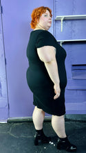 Load image into Gallery viewer, Full-body side view of a size 3 Torrid black sleeveless textured shift midi dress styled with black patent leather boots on a size 22/24 model. The photo was taken inside under flourescent and natural lighting.
