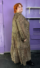 Load image into Gallery viewer, Full-body side view of a size 4X H&amp;M dark &amp; light brown and cream floral and paisley tiered maxi dress styled with black patent leather boots on a size 22/24 model. The photo was taken inside under flourescent and natural lighitng.
