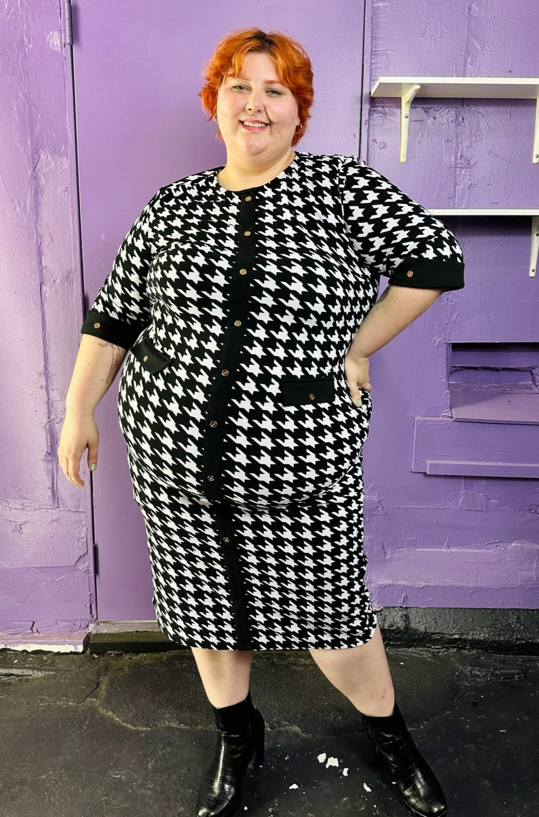 Full-body front view of a size 2X SHEIN black & white houndstooth plaid midi dress with three-quarter sleeves and gold non-functional buttons styled with black boots on a size 22/24 model. The photo was taken inside under flourescent and natural lighting.