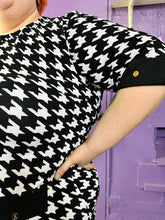 Load image into Gallery viewer, Close view of the houndstooth pattern and three-quarter length sleeve of a size 2X SHEIN black &amp; white houndstooth plaid midi dress with three-quarter sleeves and gold non-functional buttons on a size 22/24 model. The photo was taken inside under flourescent and natural lighting.

