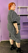 Load image into Gallery viewer, Full-body side view of a size 2X SHEIN black &amp; white houndstooth plaid midi dress with three-quarter sleeves and gold non-functional buttons styled with black boots on a size 22/24 model. The photo was taken inside under flourescent and natural lighting.
