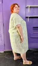 Load image into Gallery viewer, Full-body side view of a size XXL (fits up to 24 comfy) H&amp;M light green and white acid wash tie dye caftan styled with tan slides on a size 22/24 model. The photo was taken inside under fluorescent and natural lighting.
