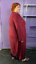 Load image into Gallery viewer, Full-body side view of a size XXXL Zelie for She maroon long sleeve longline duster styled closed over a black maxi dress on a size 22/24 model. The photo was taken inside in fluorescent and natural lighting.
