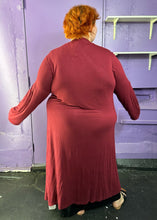 Load image into Gallery viewer, Full-body back view of a size XXXL Zelie for She maroon long sleeve longline duster styled closed over a black maxi dress on a size 22/24 model. The photo was taken inside in fluorescent and natural lighting.
