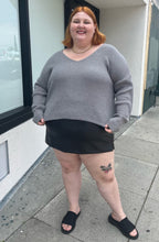 Load image into Gallery viewer, Full-body front view of a a size 4X Wild Fable gray-brown v-neck knit sweater styled over a pleather mini skirt and black slides on a size 22/24 model. The photo is taken outside in natural lighting.
