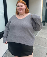 Load image into Gallery viewer, Front view of a a size 4X Wild Fable gray-brown v-neck knit sweater styled over a pleather mini skirt on a size 22/24 model. The photo is taken outside in natural lighting.
