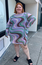 Load image into Gallery viewer, Full-body front view of a size 26 ASOS light purple, pink, brown, and green swirl pattern long sleeve mesh mini dress styled with black slides on a size 22/24 model. The photo is taken outside in natural lighting.
