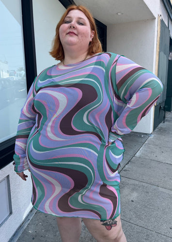 Front view of a size 26 ASOS light purple, pink, brown, and green swirl pattern long sleeve mesh mini dress on a size 22/24 model. The photo is taken outside in natural lighting.