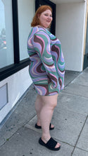 Load image into Gallery viewer, Full-body side view of a size 26 ASOS light purple, pink, brown, and green swirl pattern long sleeve mesh mini dress styled with black slides on a size 22/24 model. The photo is taken outside in natural lighting.
