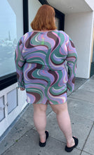 Load image into Gallery viewer, Full-body back view of a size 26 ASOS light purple, pink, brown, and green swirl pattern long sleeve mesh mini dress styled with black slides on a size 22/24 model. The photo is taken outside in natural lighting.
