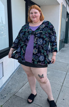 Load image into Gallery viewer, Full-body front view of a size 30/32 Maggie Barnes Vintage black, muted purple, blue, teal, and green mixed pattern floral and geometric blouse with undershirt styled with a pleather mini skirt and black slides on a size 22/24 model. The photo is taken outside in natural lighting.
