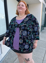 Load image into Gallery viewer, Additional front view of a size 30/32 Maggie Barnes Vintage black, muted purple, blue, teal, and green mixed pattern floral and geometric blouse with undershirt styled with a pleather mini skirt on a size 22/24 model. The photo is taken outside in natural lighting.
