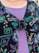Load image into Gallery viewer, Close up view of the buckle detail at the bust of a size 30/32 Maggie Barnes Vintage black, muted purple, blue, teal, and green mixed pattern floral and geometric blouse with undershirt styled with a pleather mini skirt on a size 22/24 model. The photo is taken outside in natural lighting.
