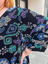 Load image into Gallery viewer, Close up view of the mixed floral and geometric pattern of a size 30/32 Maggie Barnes Vintage black, muted purple, blue, teal, and green mixed pattern floral and geometric blouse with undershirt styled with a pleather mini skirt on a size 22/24 model. The photo is taken outside in natural lighting.
