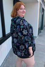 Load image into Gallery viewer, Side view of a size 30/32 Maggie Barnes Vintage black, muted purple, blue, teal, and green mixed pattern floral and geometric blouse with undershirt styled with a pleather mini skirt on a size 22/24 model. The photo is taken outside in natural lighting.
