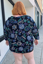 Load image into Gallery viewer, Back view of a size 30/32 Maggie Barnes Vintage black, muted purple, blue, teal, and green mixed pattern floral and geometric blouse with undershirt styled with a pleather mini skirt on a size 22/24 model. The photo is taken outside in natural lighting.
