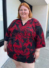 Load image into Gallery viewer, Front view of a size 3X Avenue Vintage red and black psychadelic pattern tunic blouse with a v-neck slit and bell sleeves on a size 22/24 model.
