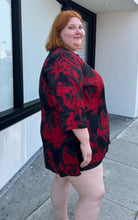 Load image into Gallery viewer, Side view of a size 3X Avenue Vintage red and black psychadelic pattern tunic blouse with a v-neck slit and bell sleeves on a size 22/24 model.
