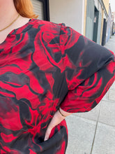 Load image into Gallery viewer, Close up view of the psychedelic pattern and sleeves of a size 3X Avenue Vintage red and black psychadelic pattern tunic blouse with a v-neck slit and bell sleeves on a size 22/24 model.
