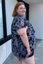 Load image into Gallery viewer, Side view of a size 30/32 Avenue black and white geometric floral flutter sleeve blouse with a ruffle detail at the neckline on a size 22/24 model. The photo is taken outside in natural lighting.
