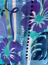 Load image into Gallery viewer, Close up view of the cool tone mixed geometric and tropical floral pattern of a size 22 Avenue vintage aqua blue, purple, green, and white tropical pattern cap sleeve blouse on a size 22/24 model. The photo is taken outside in natural lighting.
