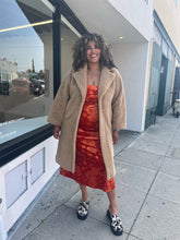 Load image into Gallery viewer, Full-body front view of a size 1X Stand Studio Teddy Bear Jacket on a size 16/18 model. They are wearing a rust orange floral dress beneath and cow print clog shoes. The model has their hands by their side to show that the jacket arms fall to their wrists. 
