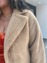 Load image into Gallery viewer, A close up of the jacket lapel and shoulder. The jacket is a light tan color and is fluffy to the touch. One button is placed under the lapel. 
