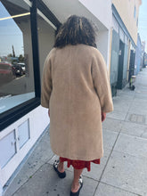 Load image into Gallery viewer, A back view of a size 1X Stand Studio Teddy Bear Jacket on a size 16/18 model. They are wearing a rust orange floral dress beneath and cow print clog shoes. The model has their arms by their side.  
