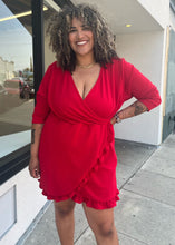 Load image into Gallery viewer, Additional front view of a size 22 Pretty Little Thing red wrap mini dress with ruffles and tulip hem styled with the sleeves pushed up on a size 16/18 model. The photo is taken outside in natural lighting.
