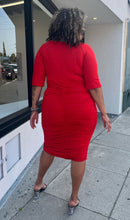 Load image into Gallery viewer, Full-body back view of a size 3X Poseshe vibrant red ruched v-neck bodycon midi dress with three-quarter length sleeves styled with black and clear heels on a size 16/18 model. The photo is taken outside in natural lighting.
