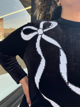 Load image into Gallery viewer, Close up view of the white sequin bow graphic on the shoulder of a size 24 Eloquii black velour long sleeve midi dress with a white sequin bow graphic at the shoulder on a size 16/18 model. The photo is taken outside in natural lighting.
