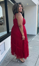 Load image into Gallery viewer, Full-body side view of a size 20 City Chic red lace and mesh halter-style gown with a tan mesh bust panel styled with black and clear heels on a size 16/18 model. The photo is taken outside in natural lighting.
