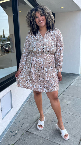 Full-body front view of a size 1/2X Brenin Newport vintage tan and white sketched floral collared a-line dress with a fabric belt styled with white heels on a size 16/18 model. The photo is taken outside in natural lighting.