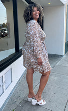 Load image into Gallery viewer, Full-body side view of a size 1/2X Brenin Newport vintage tan and white sketched floral collared a-line dress with a fabric belt styled with white heels on a size 16/18 model. The photo is taken outside in natural lighting.
