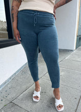 Load image into Gallery viewer, Front view of a pair of size XXXL Knix slate blue tapered drawstring pants styled with a cream tank and white heels on a size 16/18 model. The photo is taken outside in natural lighting.
