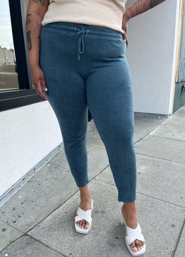 Front view of a pair of size XXXL Knix slate blue tapered drawstring pants styled with a cream tank and white heels on a size 16/18 model. The photo is taken outside in natural lighting.