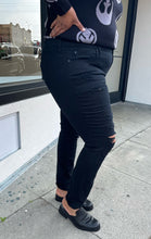 Load image into Gallery viewer, Side view of a pair of size 18 Torrid black distressed skinny jeans styled with a black and gray sweater and black loafers on a size 16/18 model. The photo is taken outside in natural lighting.
